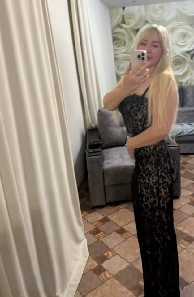 Black lace maxi dress in a mirror selfie taken in a living room with floral wallpaper