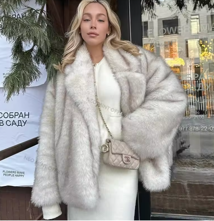 Pale fluffy faux fur jacket layered over a white knit dress with a small quilted chain bag