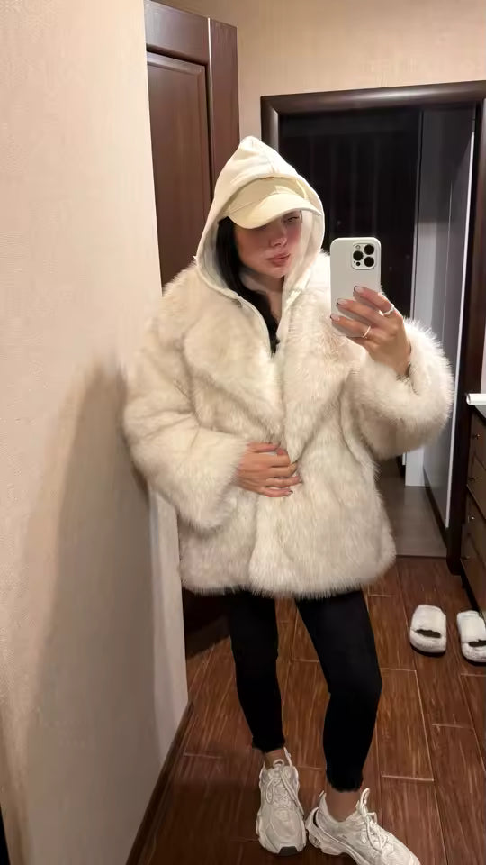 Hooded ivory faux-fur jacket worn with a cap, black leggings and white trainers in a hallway