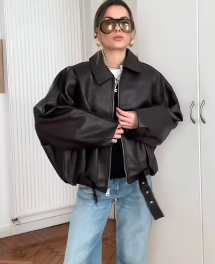 Oversized black leather zip jacket over a white tee with light blue wide-leg jeans indoors