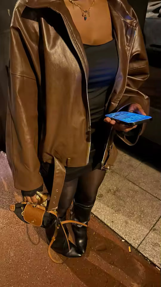 Cropped shot of an oversized brown leather jacket worn with a black skirt and knee boots