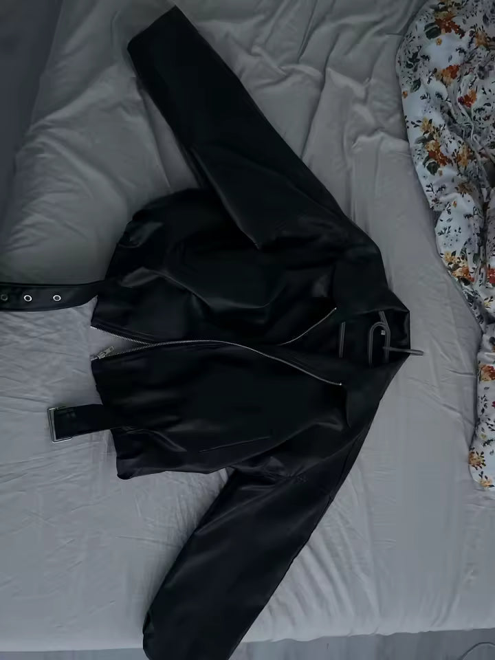 Black leather jacket with a buckled belt, laid out on white bedding