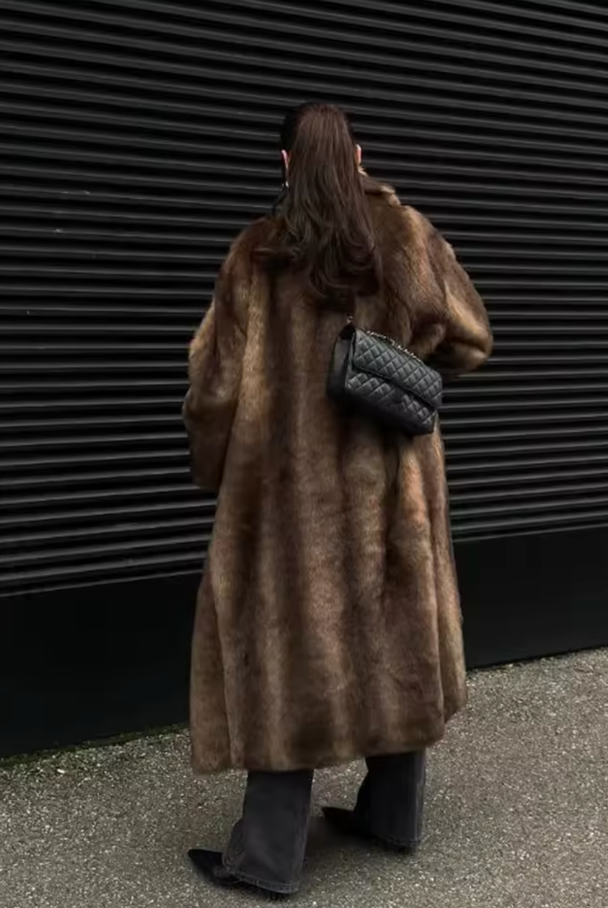 Back view of a full-length brown faux fur coat with a small quilted bag on the shoulder