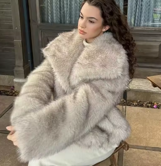 Oversized pale grey faux fur jacket with a wide collar, worn seated on a stone step