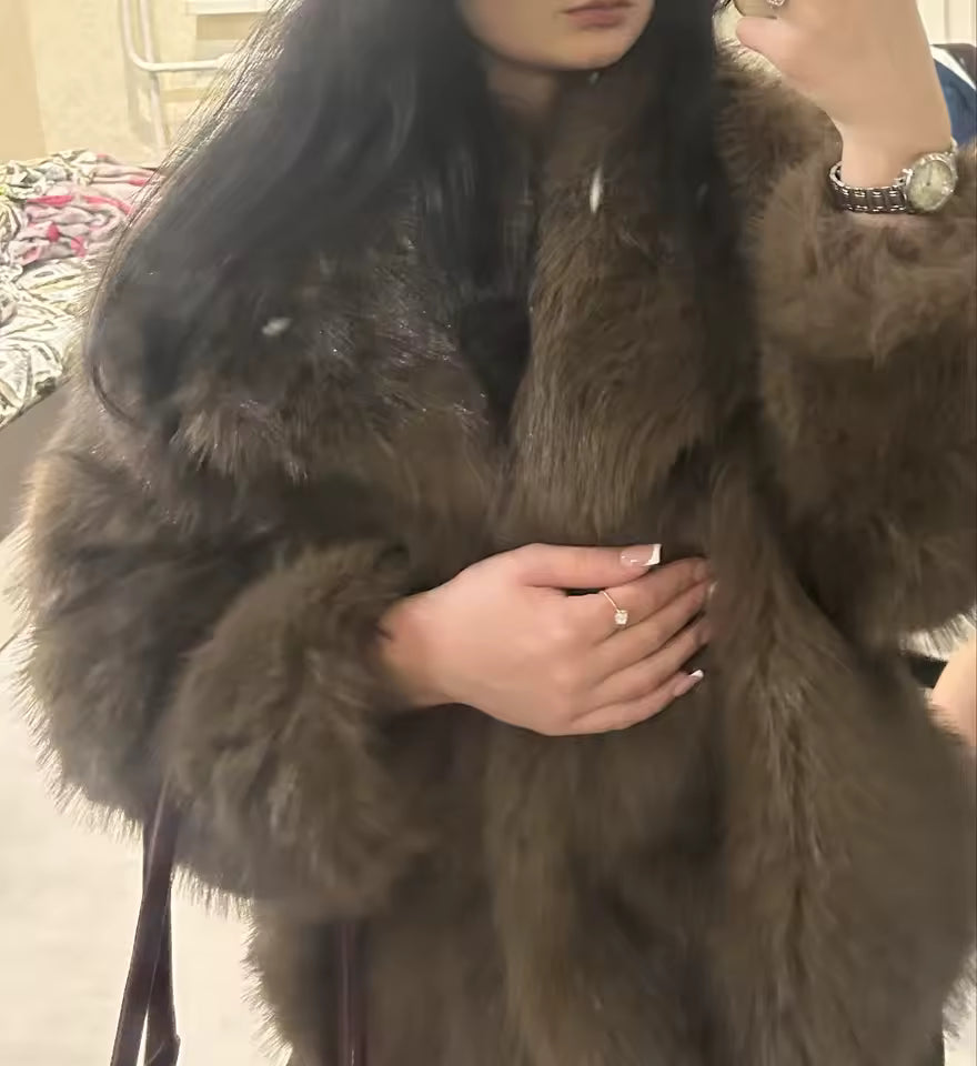 Close crop of a chocolate-brown faux-fur coat with a wide collar, worn indoors with a gold watch