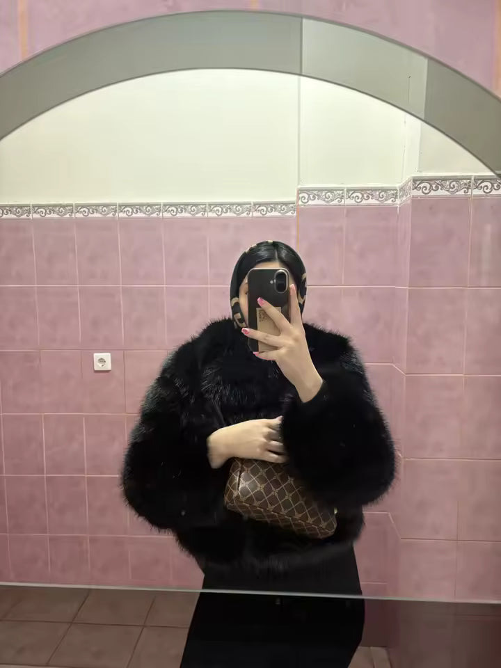 Black faux-fur jacket photographed in a pink-tiled bathroom mirror, patterned clutch in hand