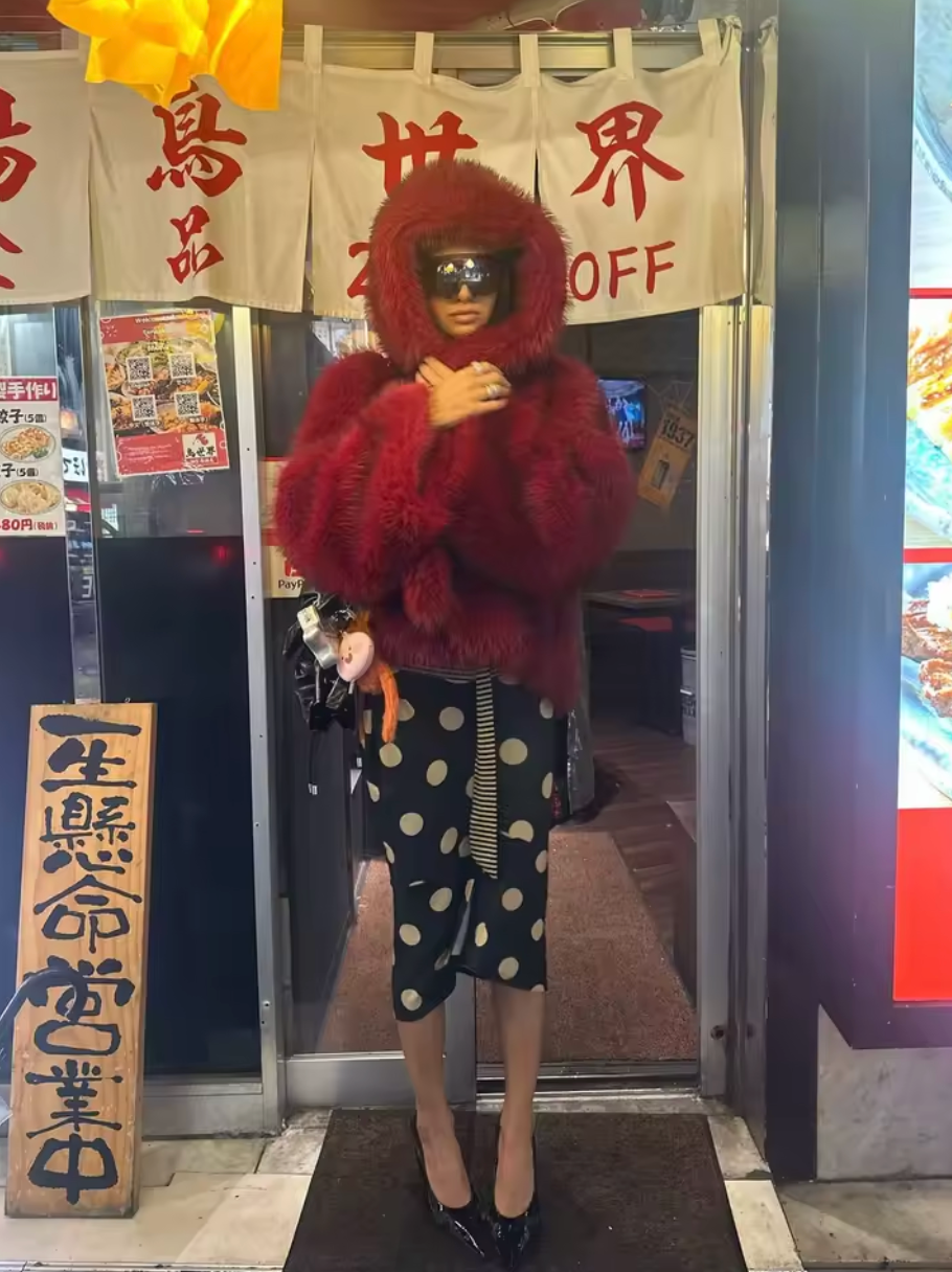 Red hooded faux fur jacket with a black polka-dot skirt outside a Japanese shopfront