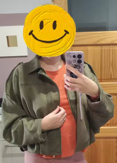 Olive suede jacket over an orange tee in a mirror selfie, face hidden by a smiley sticker