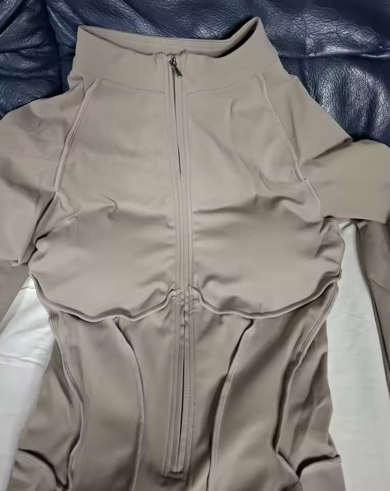 Close-up of the taupe jumpsuit's zip front and curved seams, laid on a dark leather sofa