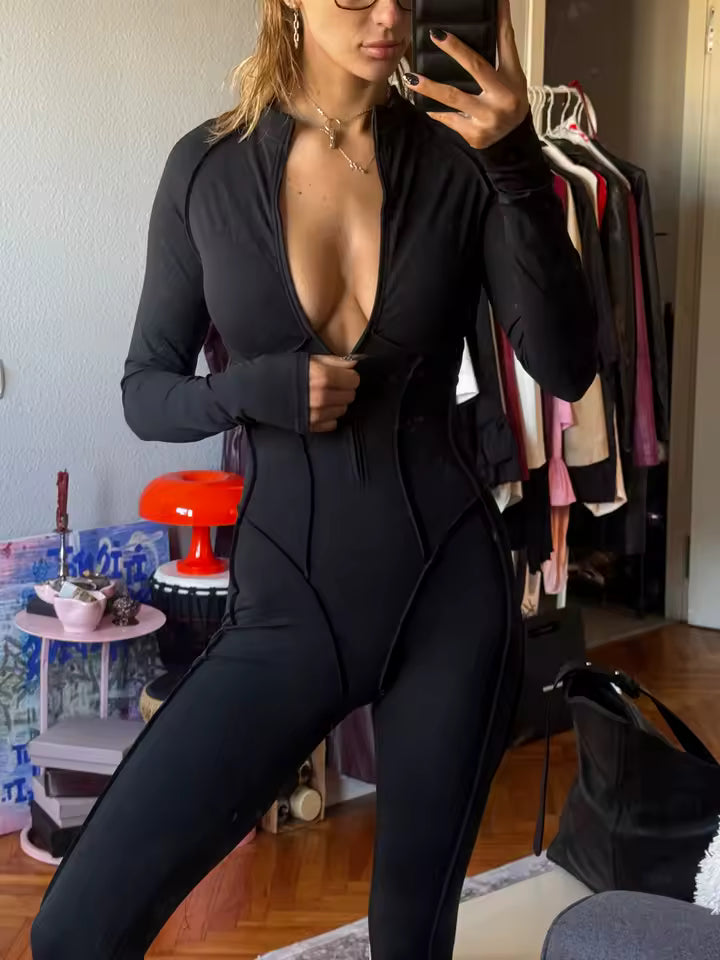 Black zip-front jumpsuit worn unzipped, mirror selfie beside a clothing rail and red lamp