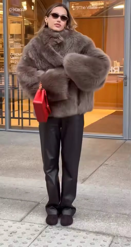 Grey faux-fur jacket with black leather trousers and a red bag, standing outside a shopfront