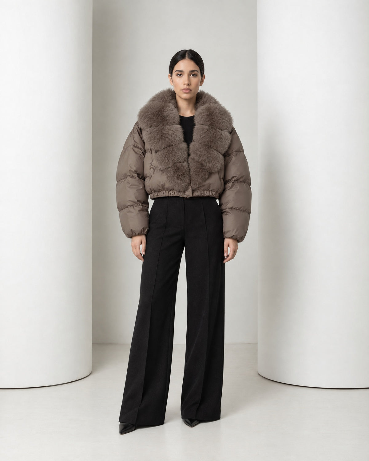 Model in the Saga cropped puffer in taupe, faux-fur shawl collar closed at the front, worn with black wide-leg trousers