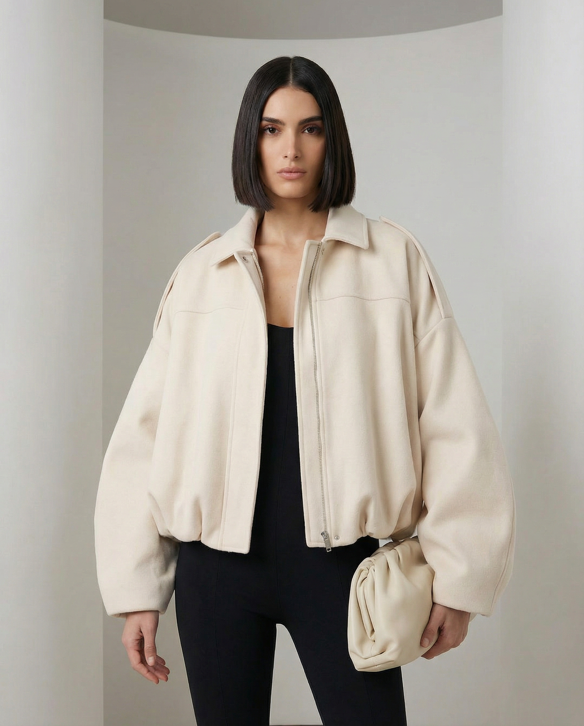 Beige Selena Jacket, a cropped zip-front bomber worn open over a black top, front view from the thigh up