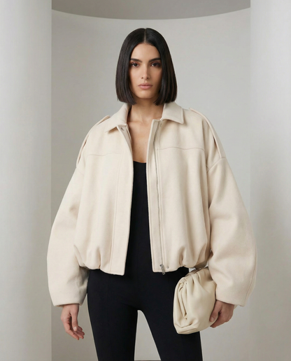 Beige Selena Jacket, a cropped zip-front bomber worn open over a black top, front view from the thigh up