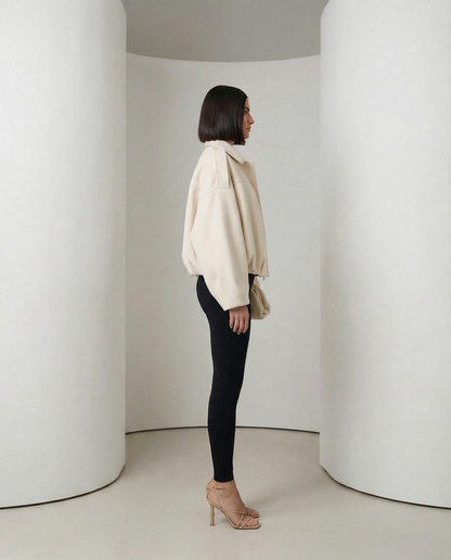 Beige Selena Jacket in a full-length side view, oversized cropped bomber over black leggings and heels