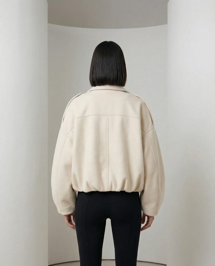 Beige Selena Jacket, a cropped zip-front bomber worn open over a black top, front view from the thigh up