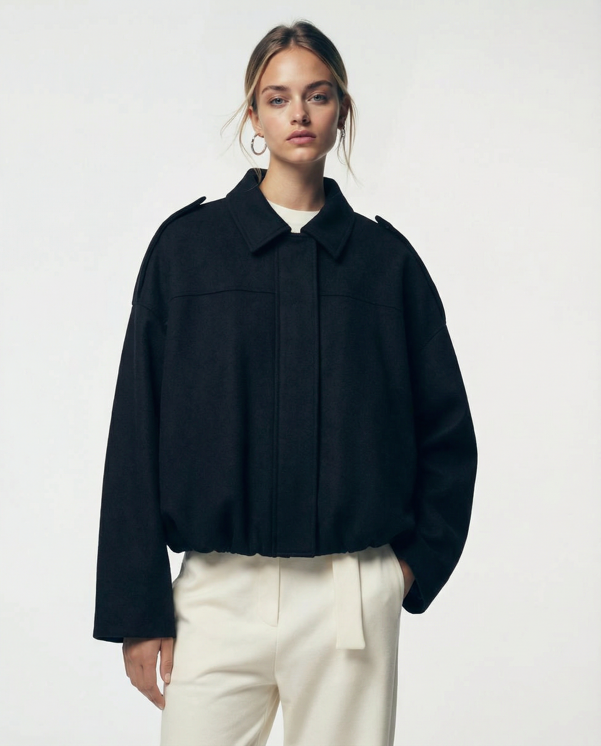 Black cropped bomber with a concealed placket front and shoulder tabs, straight-on view from the hip up