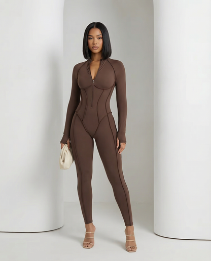 Bitter chocolate sculpting jumpsuit worn standing with a cream clutch, long sleeves and ankle hem