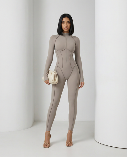 Glacier grey sculpting jumpsuit worn front on with a cream clutch, long sleeves and ankle hem