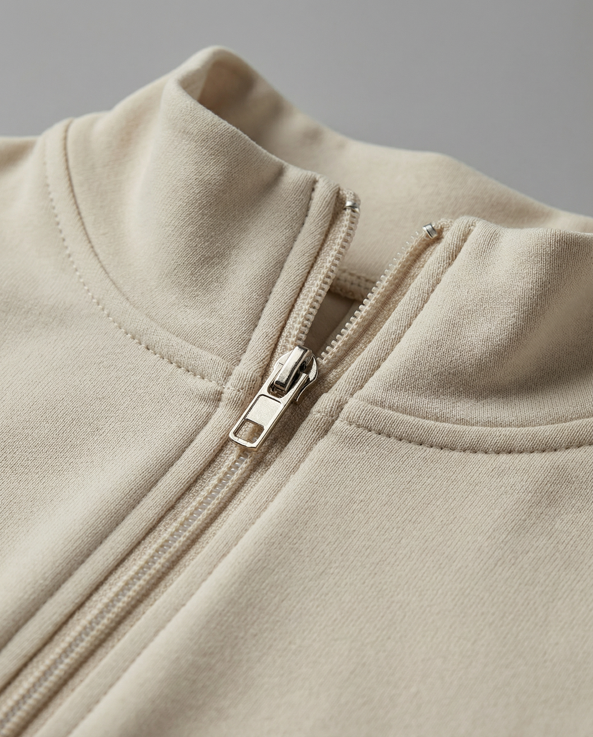 Close crop of a cream zip-front knit jacket, showing the mock collar and silver zip pull