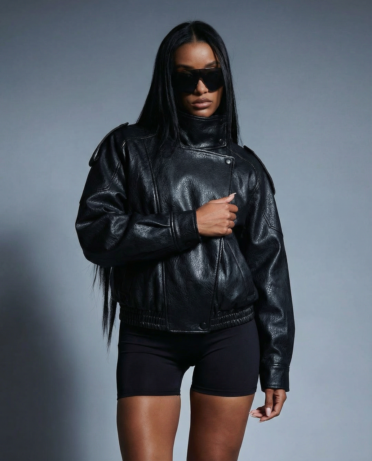 A black leather biker jacket worn over bike shorts and sunglasses on a grey studio backdrop