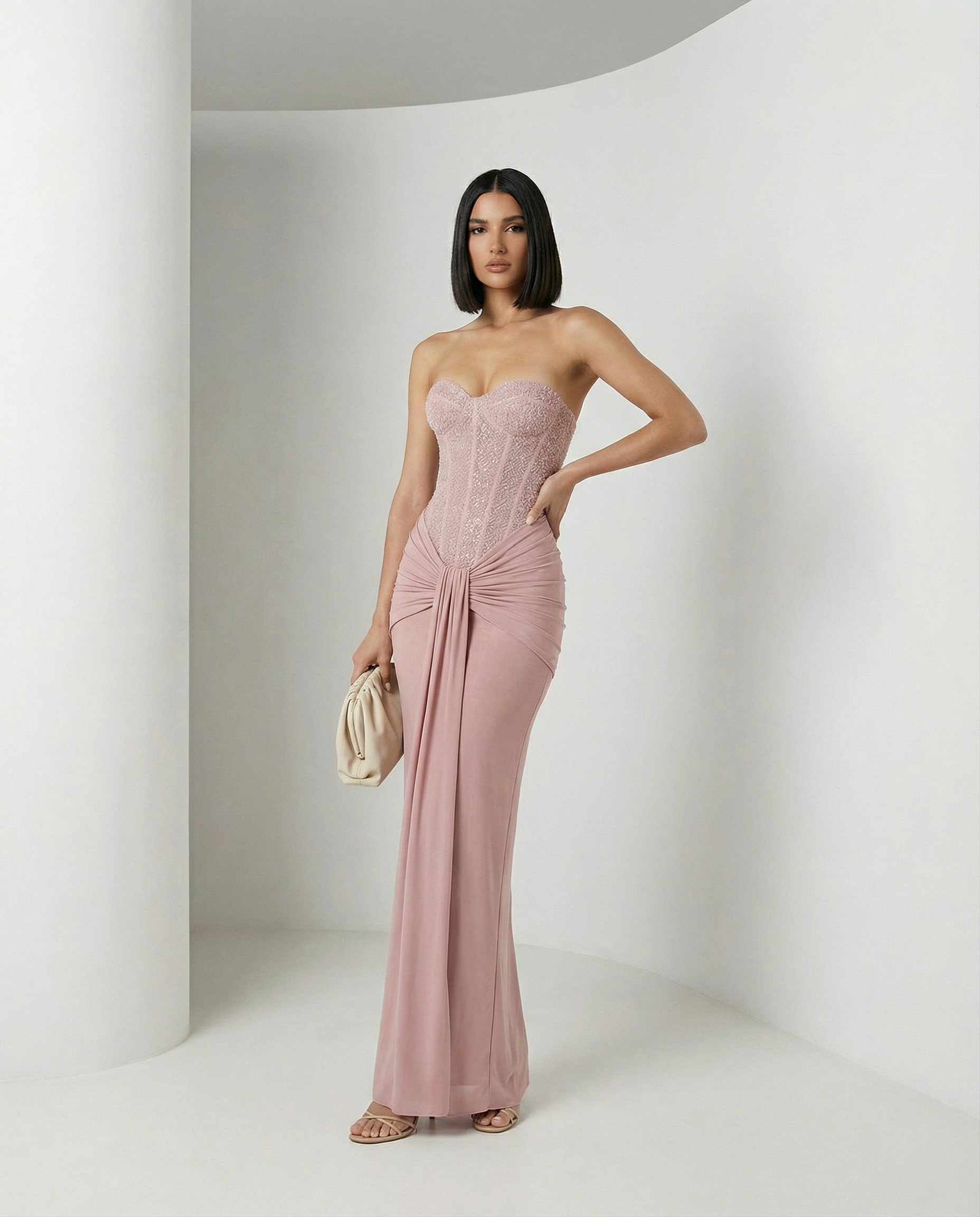 Dusty pink strapless corset maxi with a knotted hip drape, hand on hip, full length front view