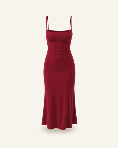 The Siv midi slip dress in burgundy, narrow straps, straight neckline and a fluted hem, alone on a bone background