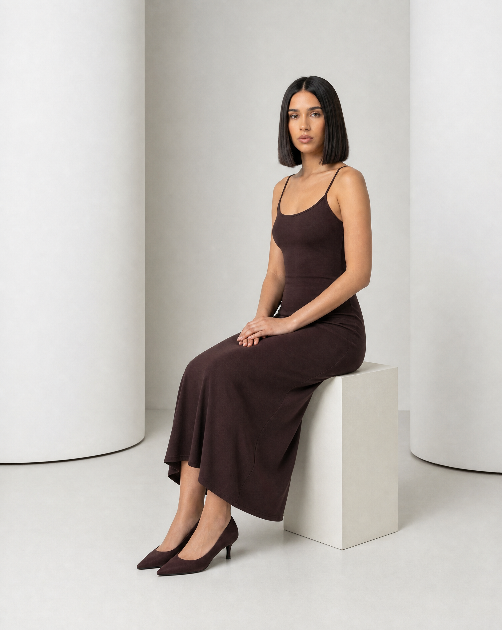 Model seated in the Siv espresso slip dress, showing where the midi hem falls on the shin