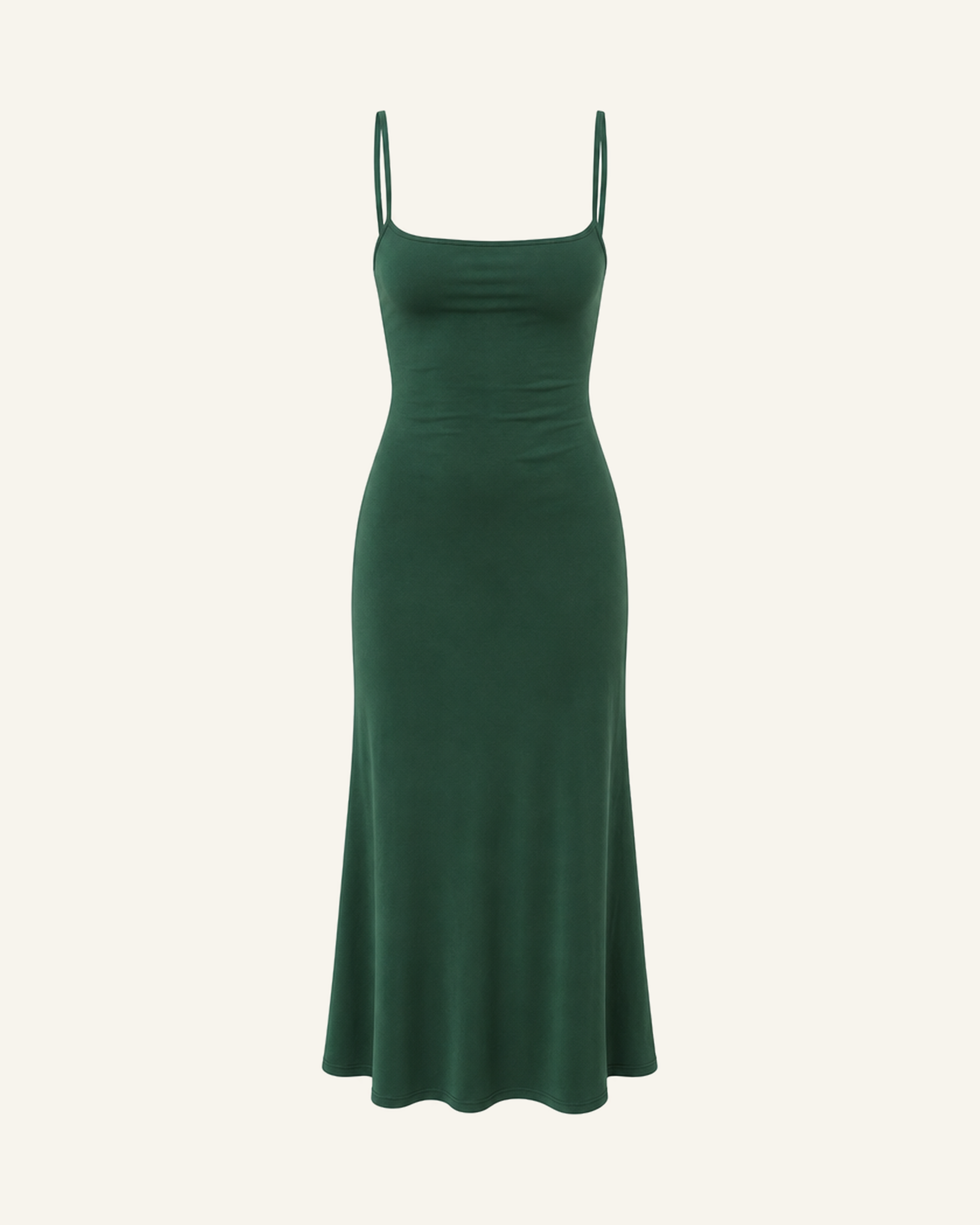 The Siv midi slip dress in forest green, narrow straps, straight neckline and a fluted hem, alone on a bone background
