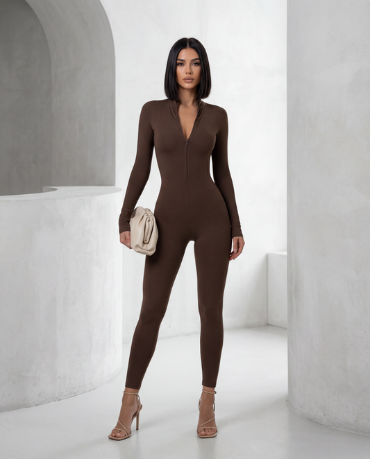 Bitter chocolate Skadi jumpsuit with half-zip mock neck, full length front view with a cream clutch