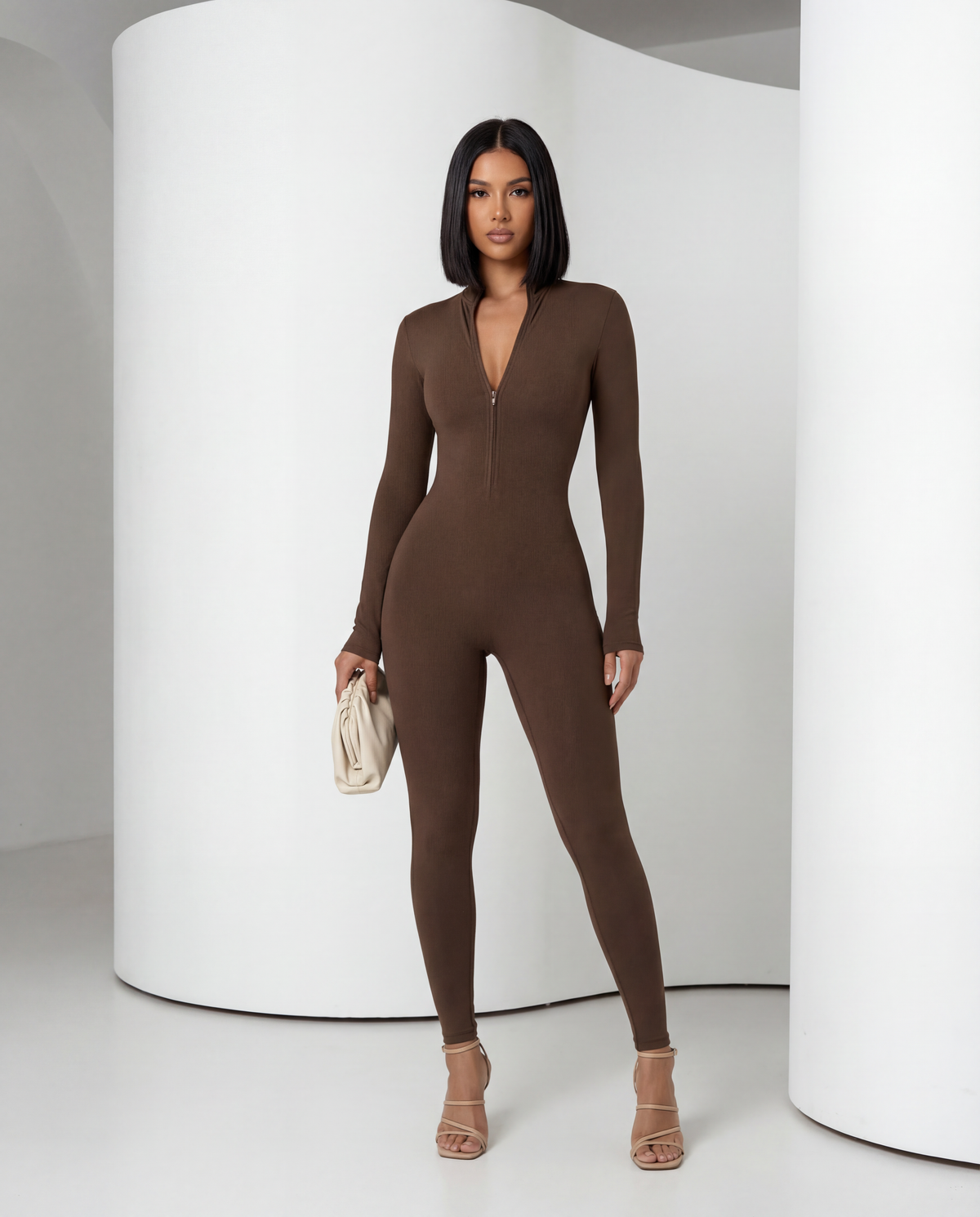 Bitter chocolate jumpsuit worn with nude heels, front view against a curved white wall