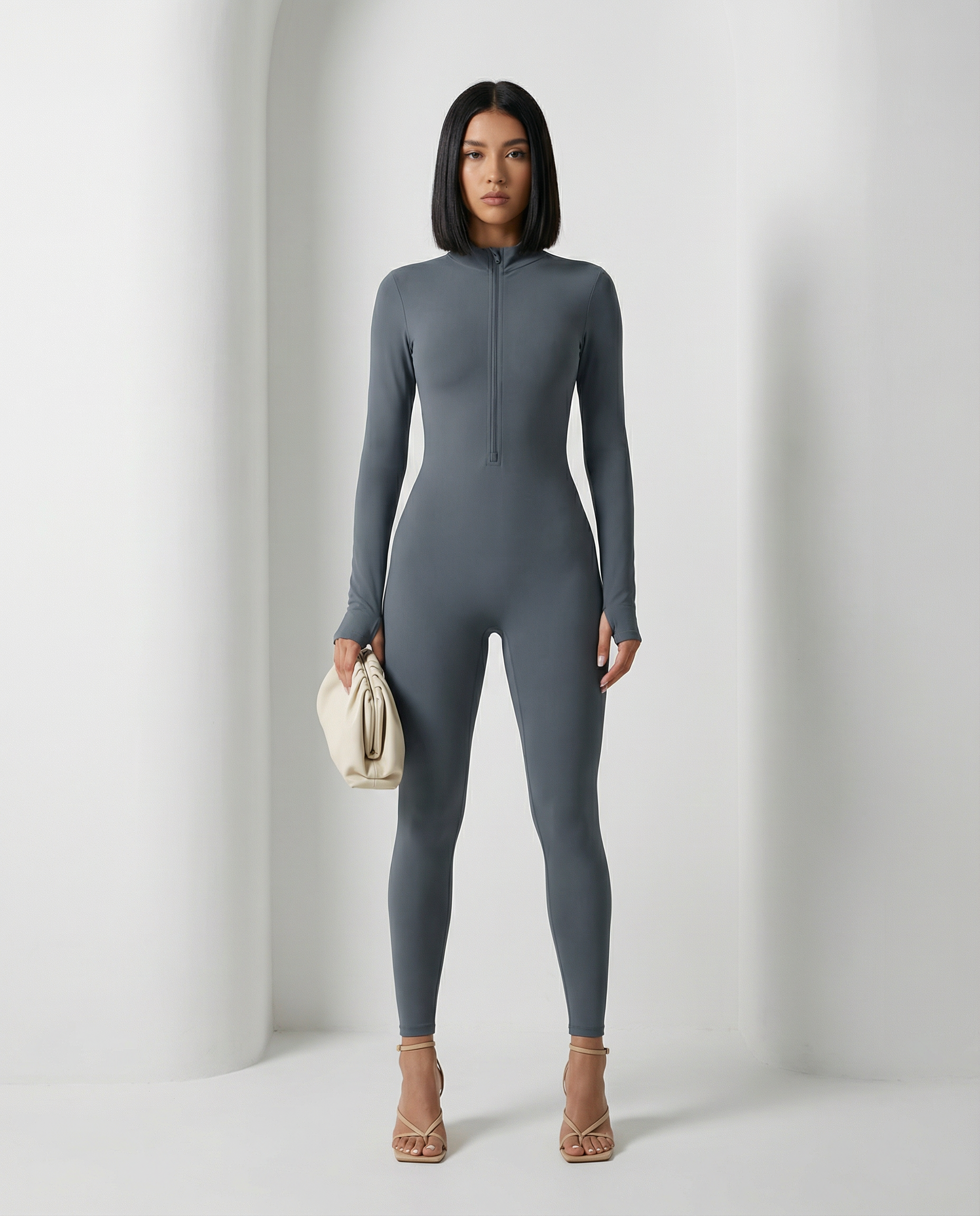 Slate grey Skadi jumpsuit with half-zip neck, full length front view with a cream clutch