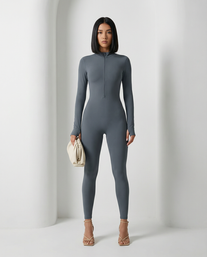 Slate grey Skadi jumpsuit with half-zip neck, full length front view with a cream clutch