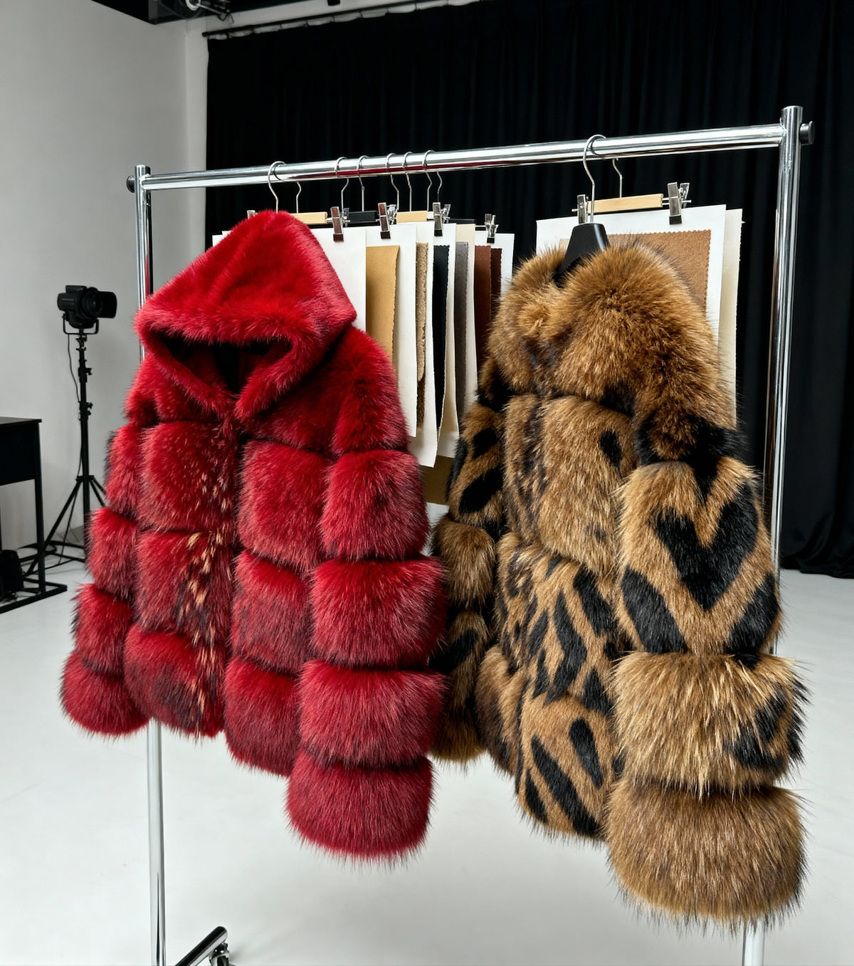 Red hooded and leopard faux-fur coats on a studio rail beside hanging fabric swatches