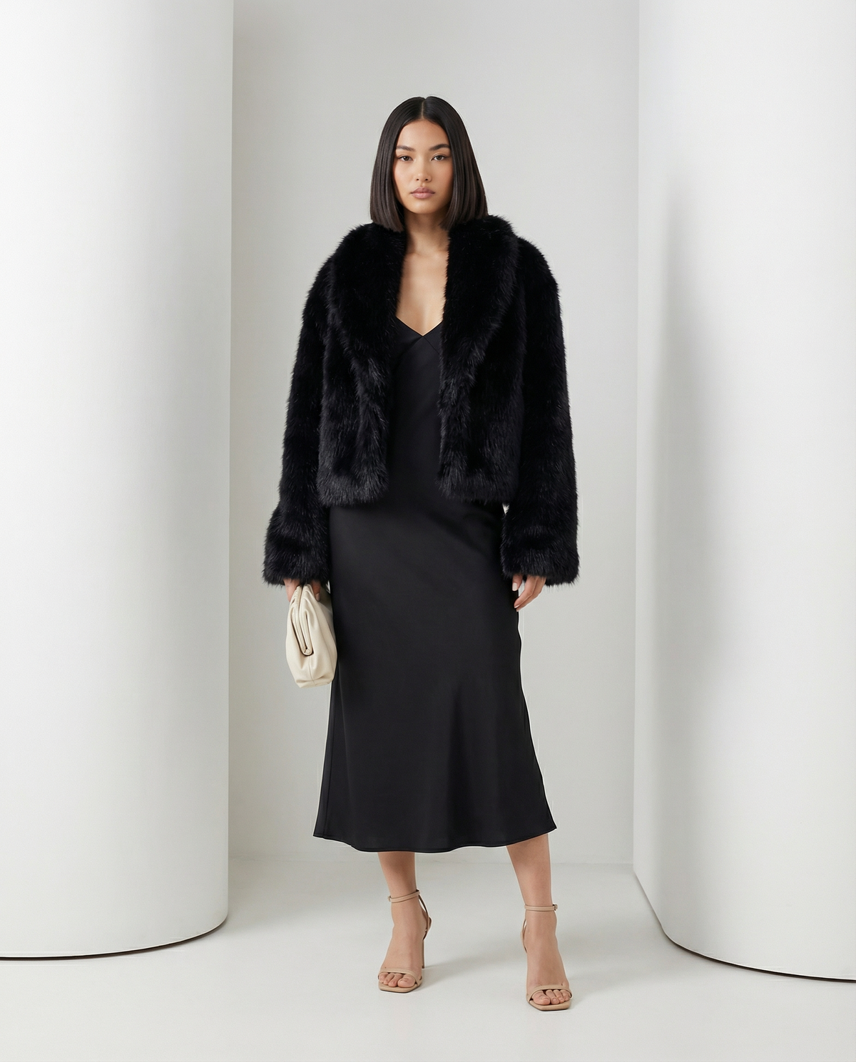 Vera faux-fur jacket in black with a soft shawl collar, styled over a black V-neck slip dress