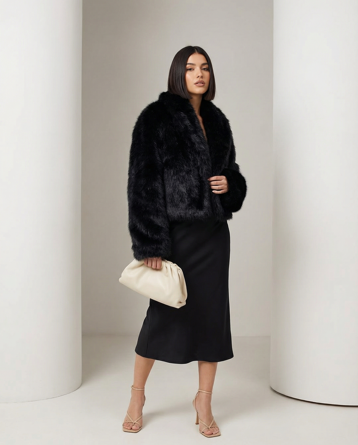 Black faux-fur jacket worn open with turned-back cuffs, three-quarter stance with a cream pouch
