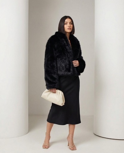 Black faux-fur jacket worn open with turned-back cuffs, three-quarter stance with a cream pouch