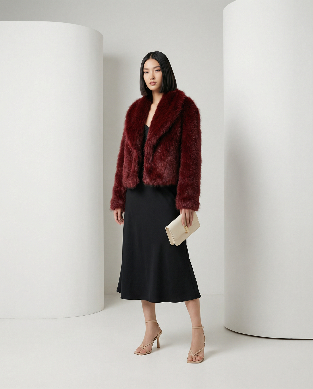 Deep burgundy faux-fur jacket worn open, mid-stride with a cream clutch and black midi skirt