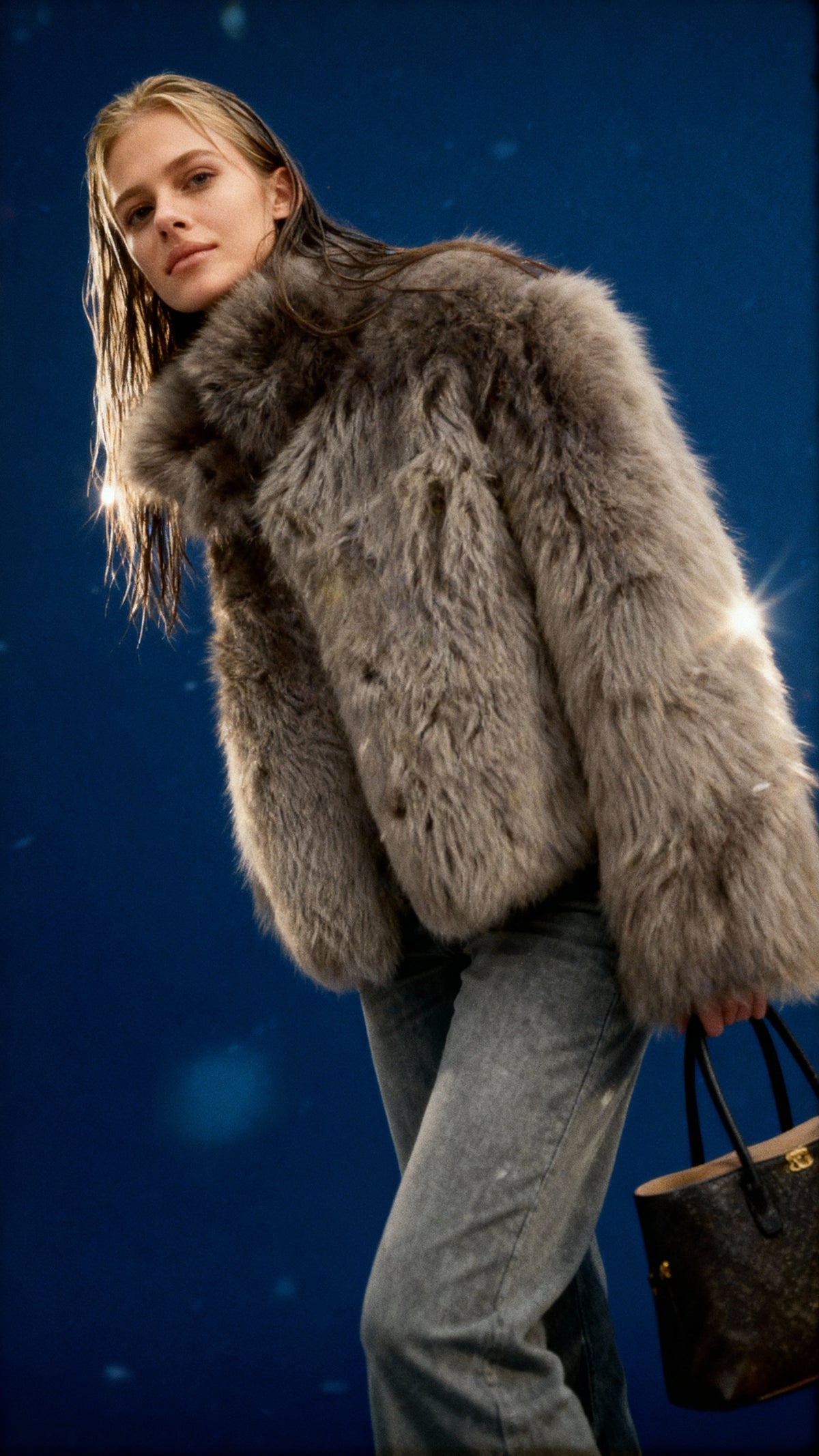 Silver-grey cropped faux-fur jacket worn with straight-leg jeans against a deep blue night sky