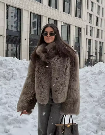 Cropped taupe faux-fur jacket styled with jeans in falling snow, waist-up street shot